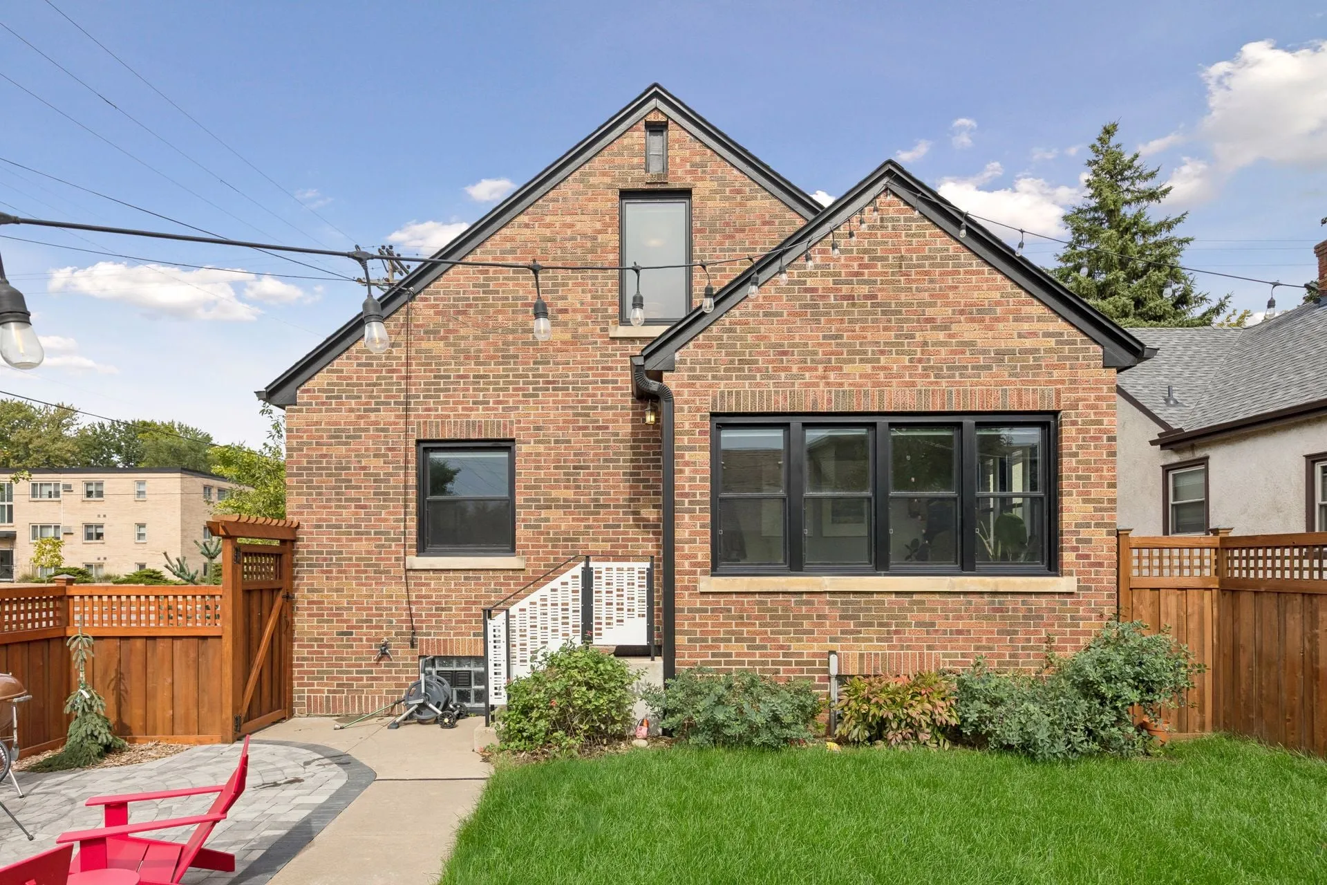 Back of a brick house with black trim along both gables and a black gutter and downspout, between stained cedar fences