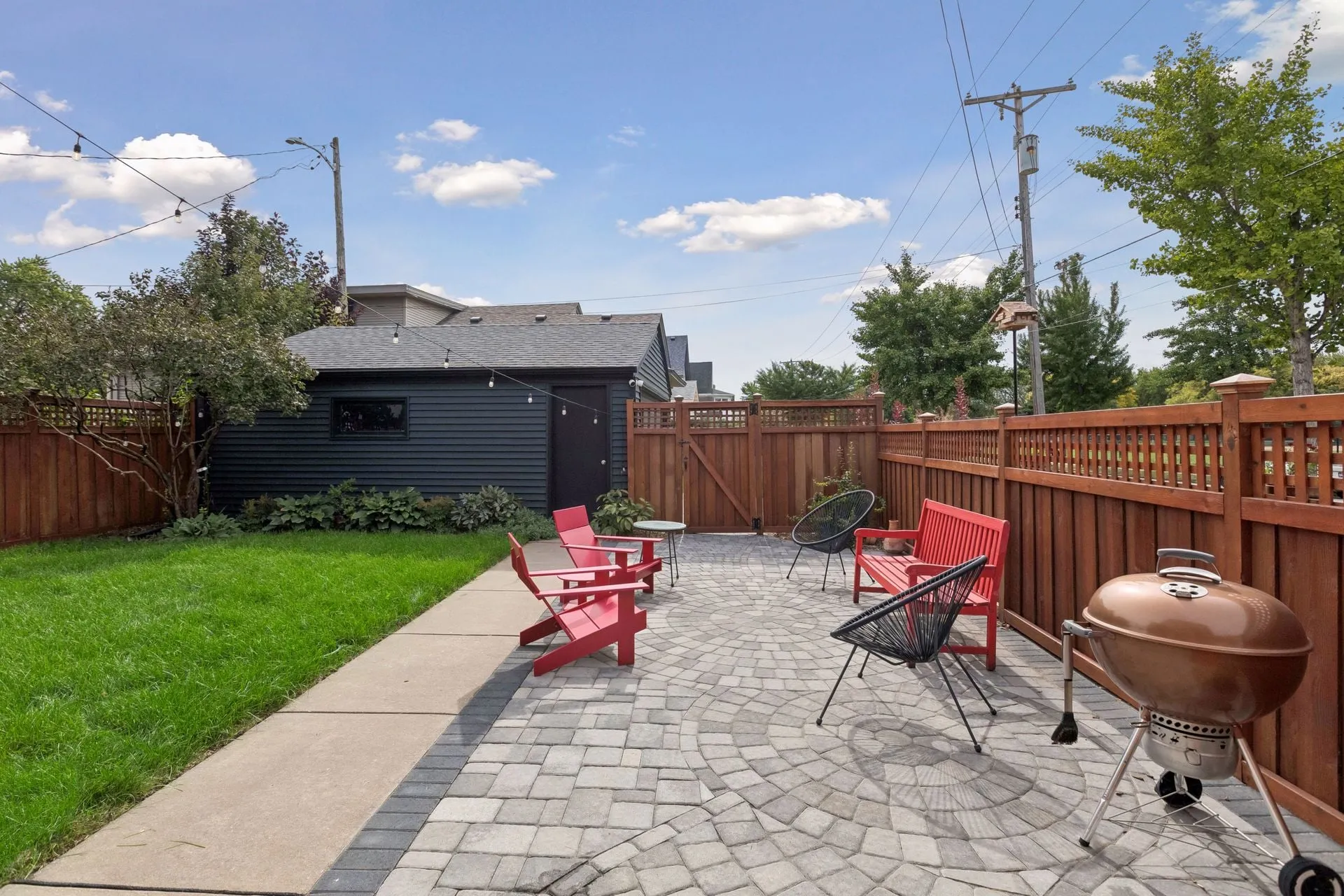 Patio and lawn inside a stained cedar fence and gate, with a charcoal-sided garage at the back