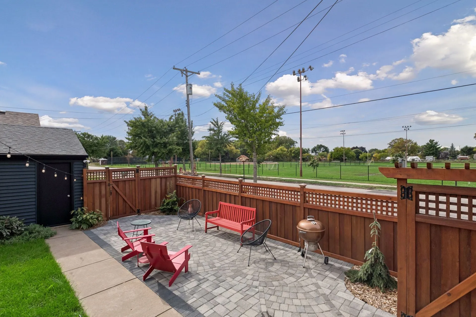 Stone patio enclosed by a stained cedar fence with a lattice top and a gate, next to a dark garage