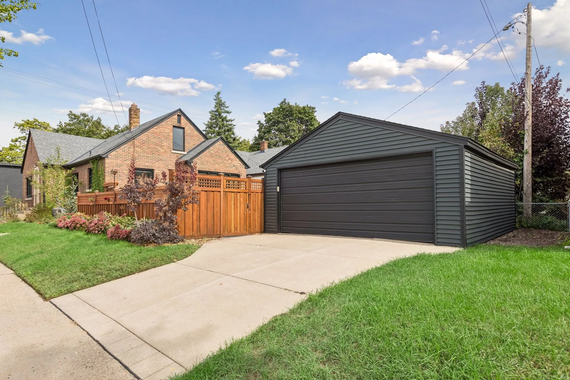 Detached garage with charcoal siding and a matching garage door at the end of a driveway, beside a stained cedar privacy fence