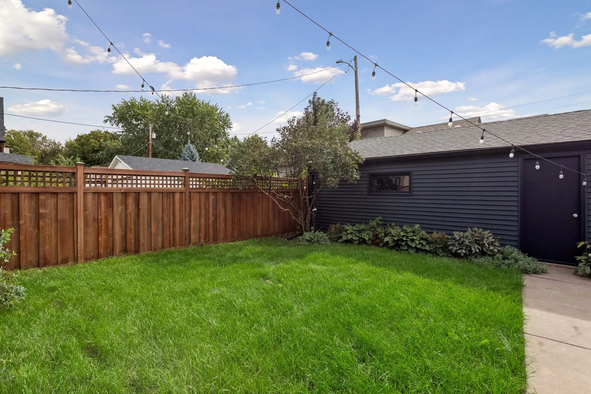 Lawn bordered by a stained cedar fence, with the charcoal-sided garage and its black side door