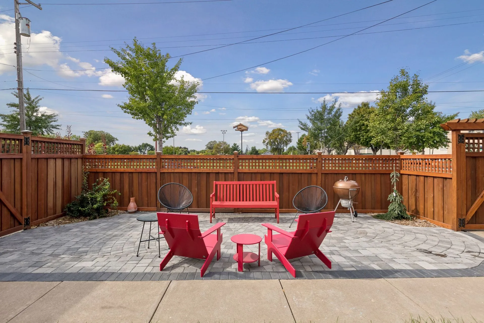 Stained cedar privacy fence with a lattice top and gates, around a stone patio with red chairs and a bench